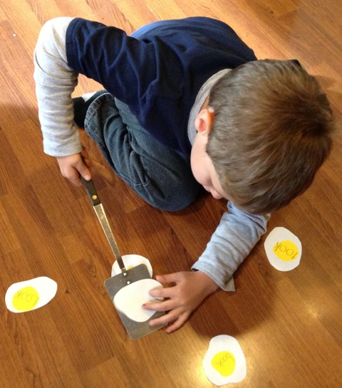 Andrew is using a pancake flipper to pick up the correct sight words written on eggs.