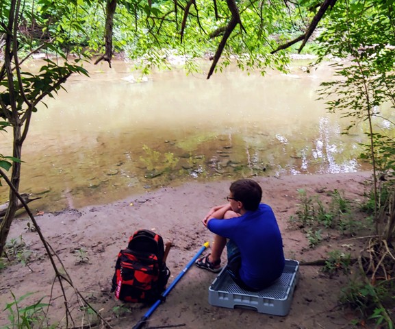 Boy sitting on creek bank watching the water.