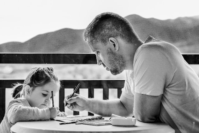 Dad and daughter homeschooling at table.